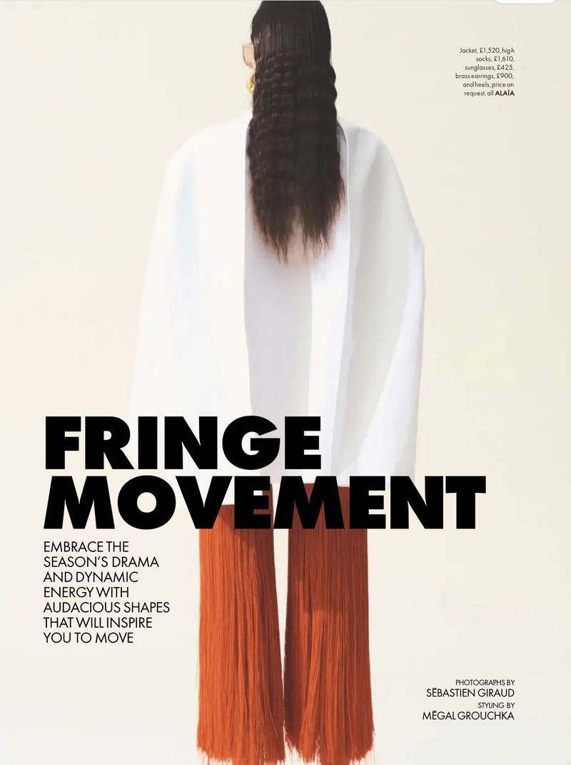 Fashion editorial shot of a woman from the back wearing a white top and orange fringe pants against a cream background.