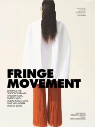 Model from behind wearing a white jacket and orange fringed pants against a seamless light background.