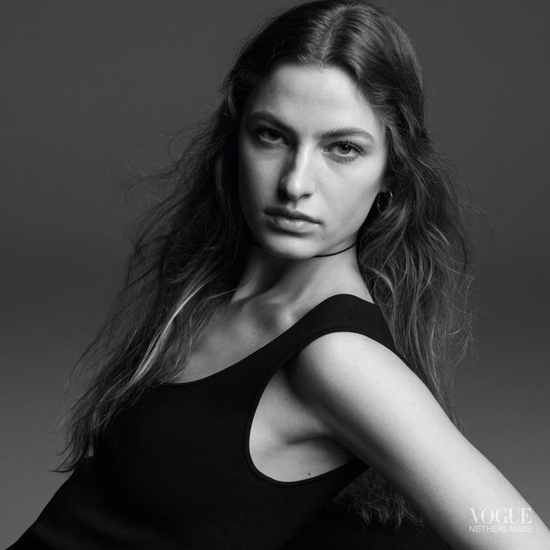 Black and white portrait of a woman wearing a dark sleeveless top against a solid grey studio background.