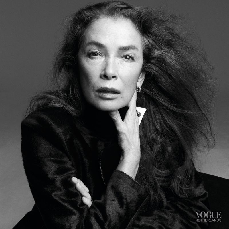 Portrait of an older woman with long dark hair wearing a black top against a grey seamless background for Vogue Netherlands