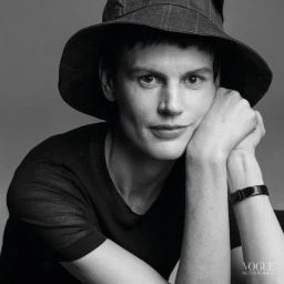 Black and white portrait of Saskia de Brauw wearing a dark hat and t-shirt, resting chin on hands