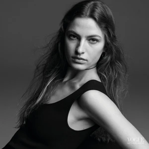 Black and white portrait of a woman wearing a dark sleeveless top against a solid grey studio background.