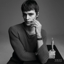 Portrait of a man wearing a ribbed sweater holding a carrot against a grey studio backdrop for Vogue Netherlands