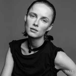 Monochrome portrait of a woman wearing a dark top and heart choker necklace against a grey seamless studio background.
