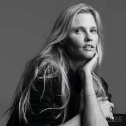 Monochrome portrait of model Lara Stone with long blonde hair resting chin in hand against a neutral grey studio background