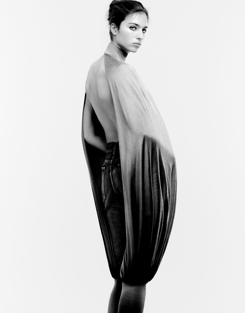 Monochrome studio shot featuring a slender adult woman in a flowing top and dark denim jeans, gazing over her shoulder.