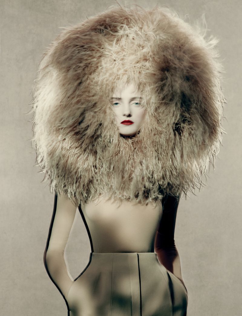 A fashion portrait features a woman in a beige dress and large feathered headpiece, looking directly at the camera against a neutral background.