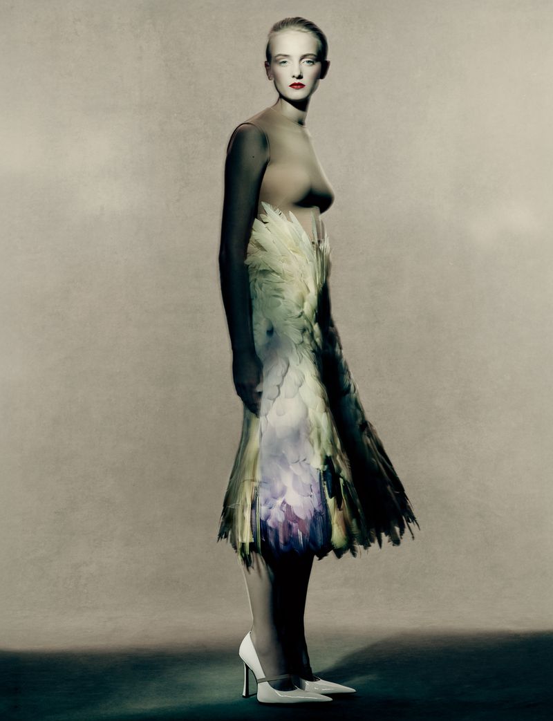 Woman in high heels wearing a dress made of feathers in a studio setting, artistic fashion photography. Neutral background, artful style.