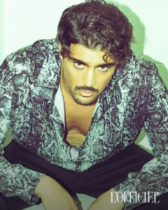 Man with dark curly hair and facial hair wearing a snakeskin patterned shirt in an editorial portrait for L'Officiel Hommes Italia.