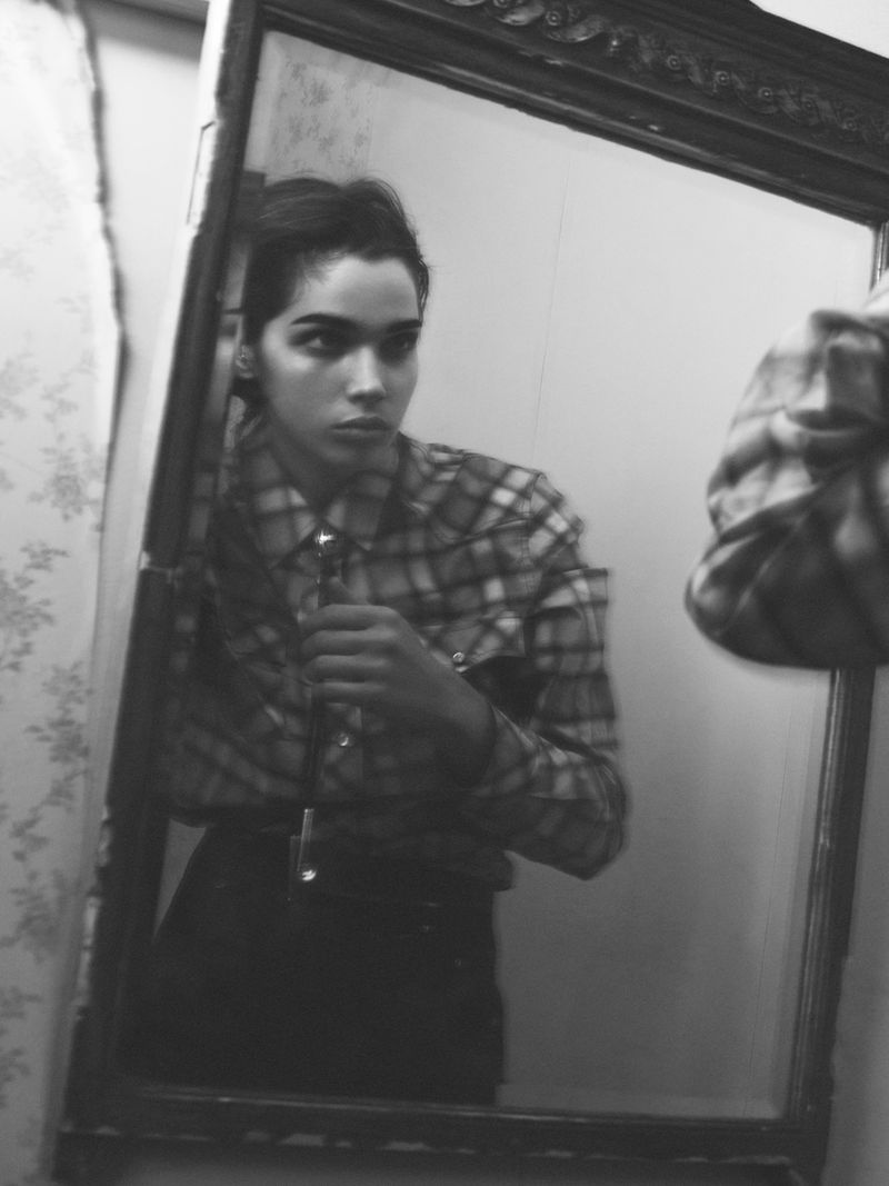 Indoor portrait of a young adult woman in a plaid western shirt, reflected in a vintage ornate mirror in black and white.