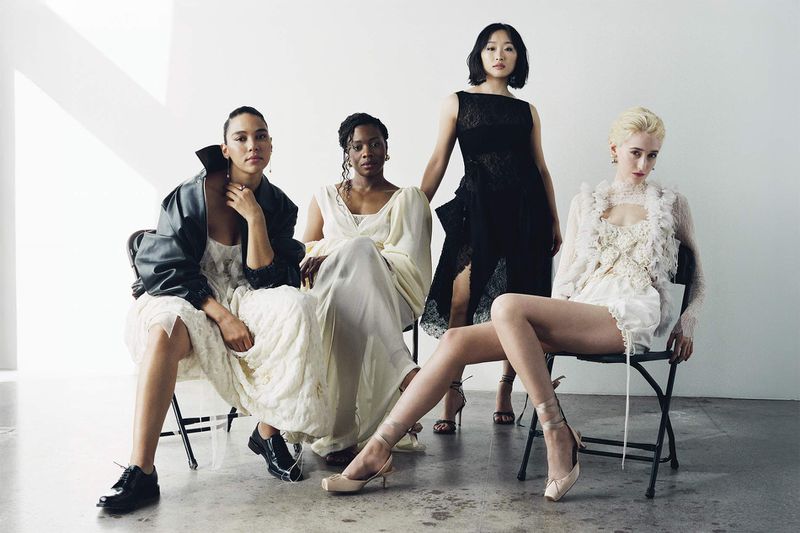 Four women sit in a bright studio wearing dresses in black and cream tones. A modern fashion editorial featuring diversity and style.