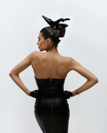 Model wearing a black leather dress and gloves with a stiletto heel hair sculpture against a plain white background