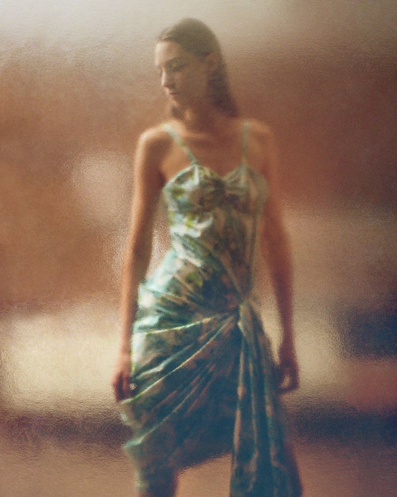 Woman in a floral dress with a draped skirt standing indoors with soft lighting, creating a dreamy and feminine aesthetic.