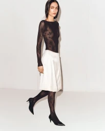 Model in black lace top and white skirt posing against a seamless white background for COS S/S 26