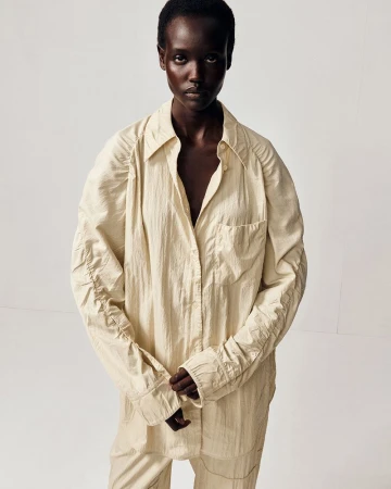 Model wearing a cream textured button-down shirt against a plain white studio background for COS S/S 26