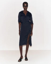 Model wearing dark sunglasses and a dark midi dress standing against a light seamless studio backdrop