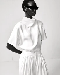 Model wearing dark sunglasses and a white high-neck top against a plain white studio background for COS S/S 26