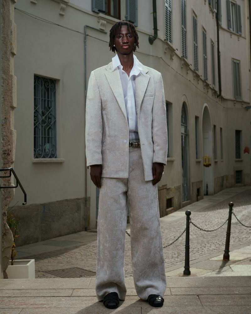 Man poses in an elegant off-white suit against an old European city street backdrop. Fashion editorial showcasing modern tailoring.
