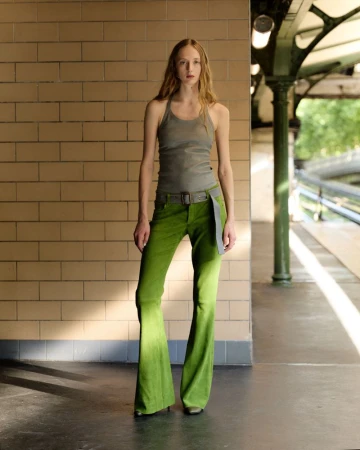 Model standing on a tiled subway platform wearing a grey tank top and green flared trousers for Stouls lookbook