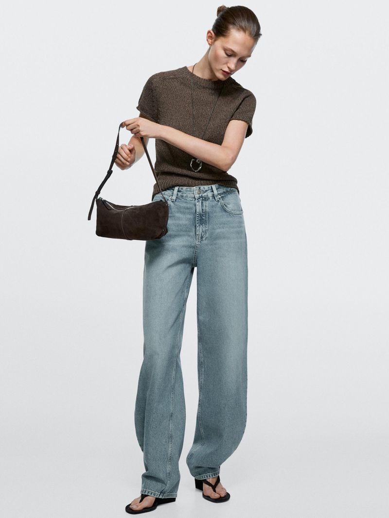 Fashion shoot features an adult female model wearing a brown short-sleeve shirt, light blue jeans, and black sandals, posing in a studio.
