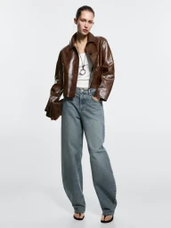 Model wearing a brown leather jacket and blue denim jeans against a white seamless background