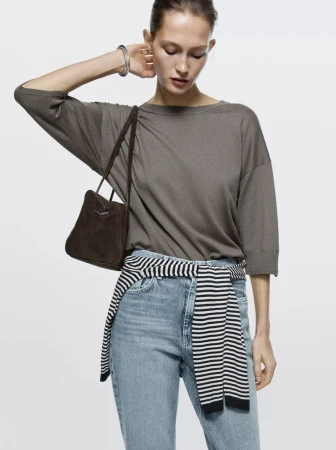 Model wearing a taupe top and light blue denim jeans with a dark brown handbag against a white background