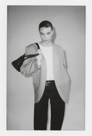 Model in blazer holding a black handbag against a grey studio backdrop for H&M SIMPLICITÉ