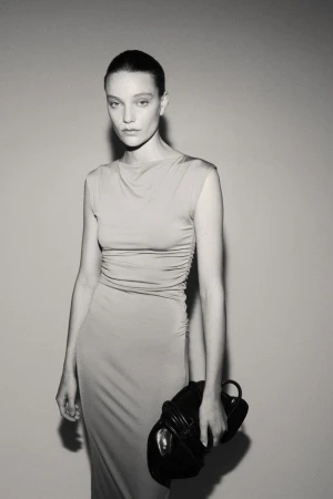 Monochrome portrait of a woman in a fitted dress holding a structured leather handbag against a plain background in a studio.