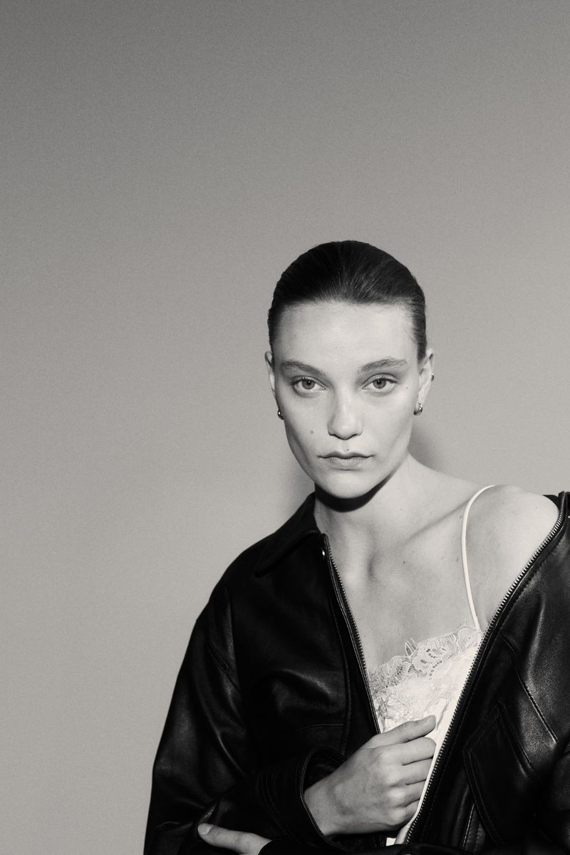 Monochrome portrait of a woman wearing a jacket and lingerie, posing against a plain background with soft, diffused lighting.