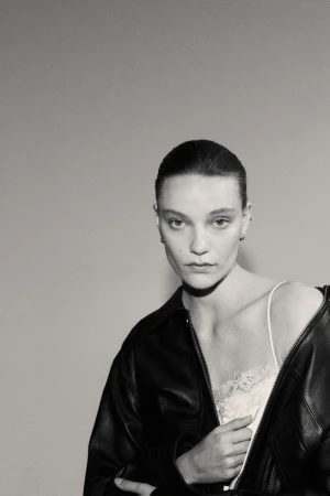 Monochrome portrait of a woman wearing a jacket and lingerie, posing against a plain background with soft, diffused lighting.