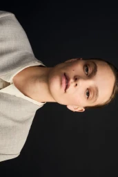 Portrait of a model wearing a grey blazer against a black seamless studio background.