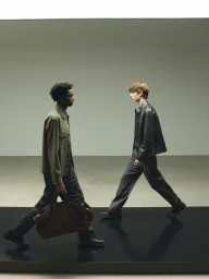 Two male models walking across a glossy dark runway platform against a neutral grey studio background for Massimo Dutti