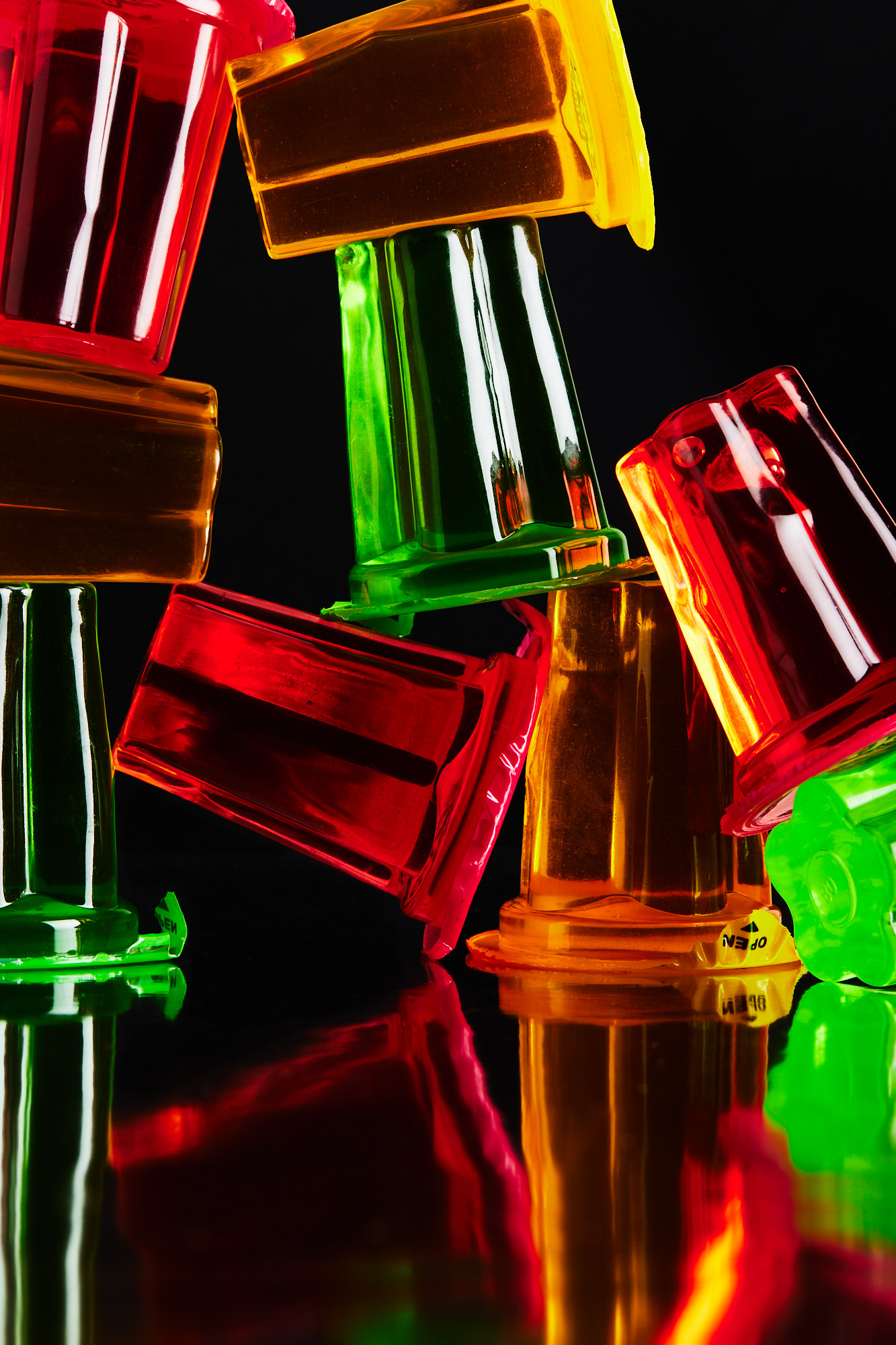 Stack of vibrant, translucent plastic cups in red, yellow, green, and orange hues against a stark black background, creating a visually striking still life.