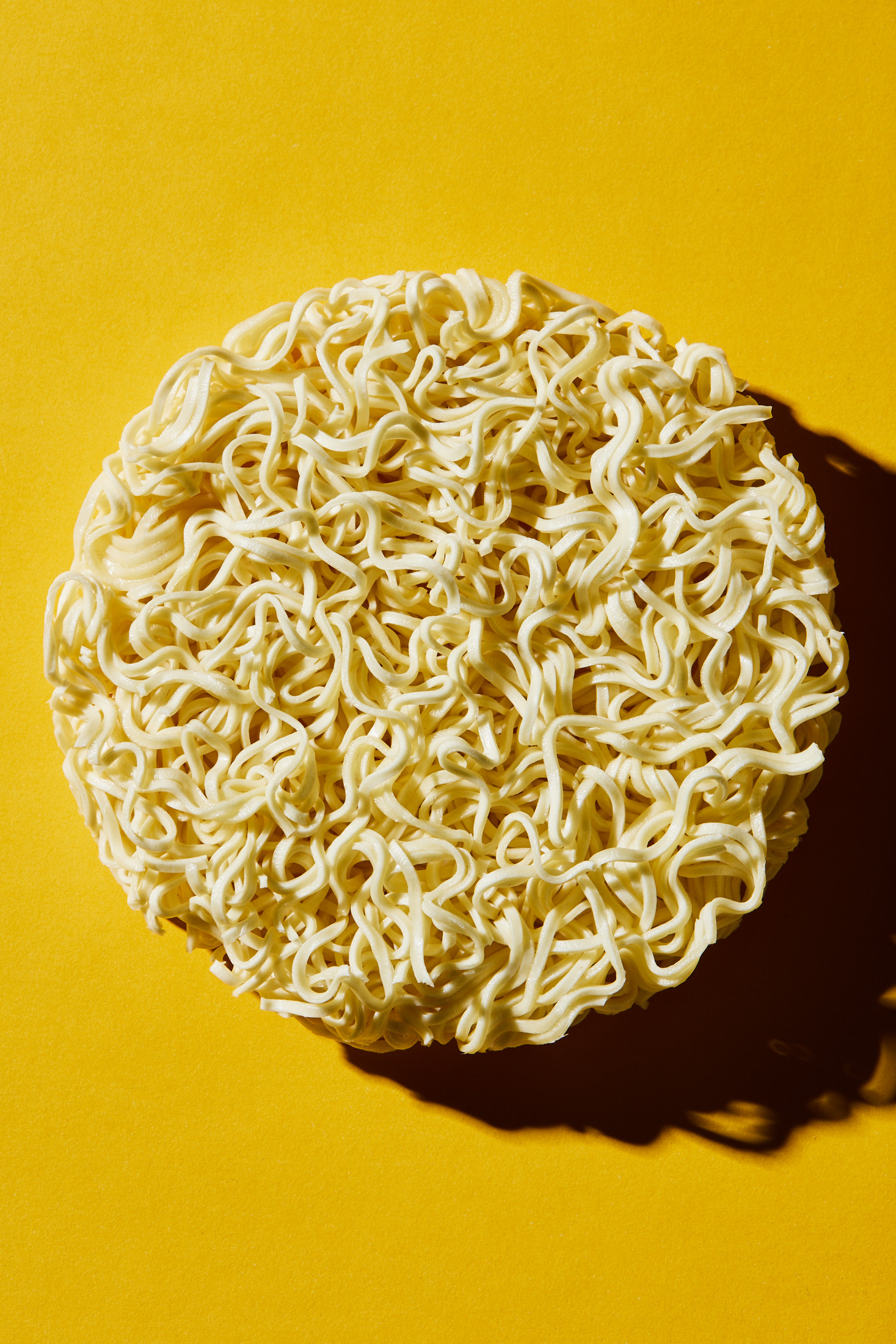 Overhead shot of a disc of dry ramen noodles on a solid yellow background, creating a simple, vibrant food still life.