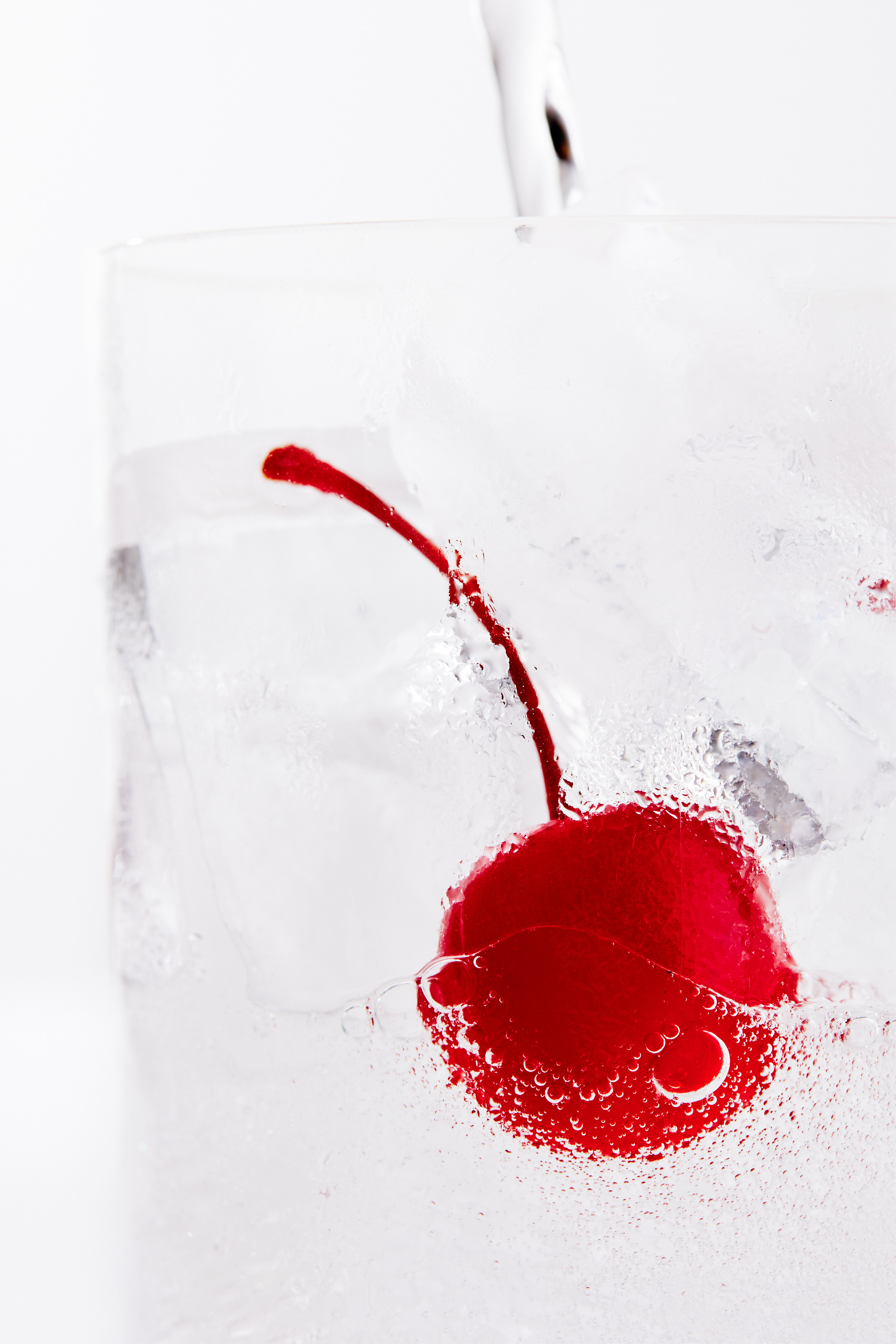 Macro shot of a red cherry suspended in a glass of soda water with ice cubes, showcasing bright color and refreshing drink appeal.