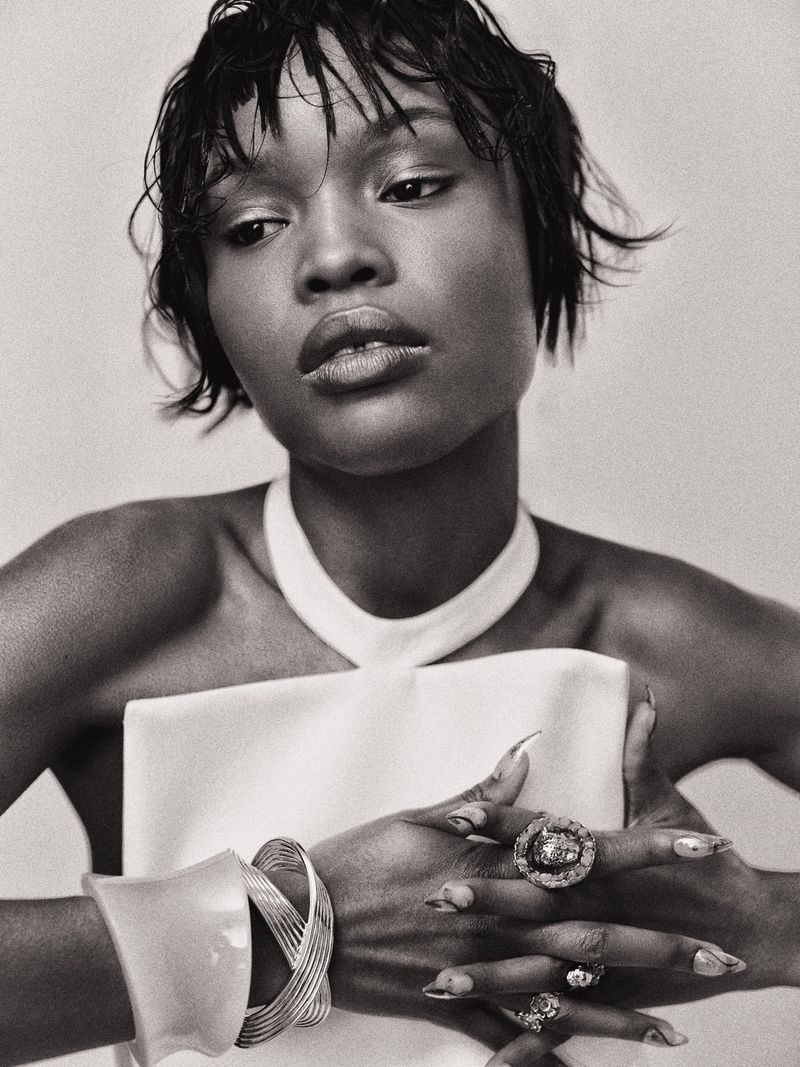 Monochrome portrait of an African-American woman with short hair, wearing a white dress and statement jewelry, looking off-camera.