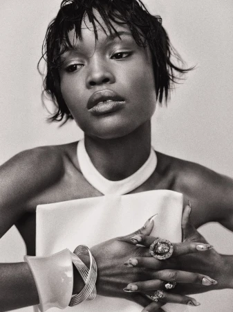 Monochrome portrait of an African-American woman with short hair, wearing a white dress and statement jewelry, looking off-camera.