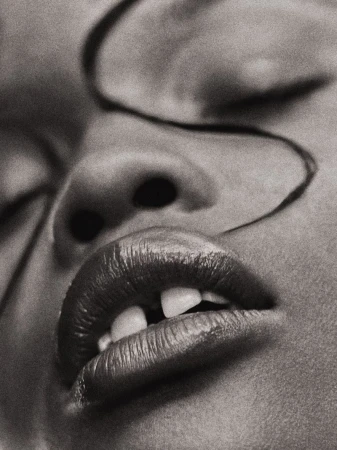 Monochrome close-up of a person's face featuring lips, teeth, nose, closed eyes, and a strand of hair against a neutral background.