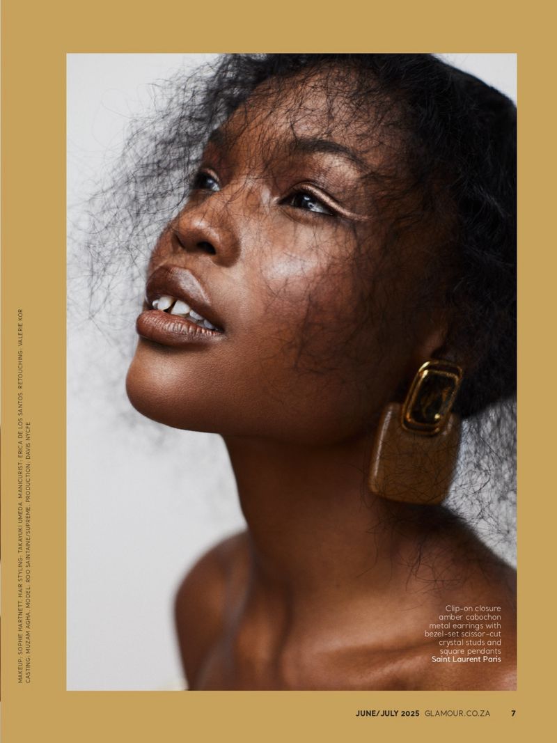 Close-up fashion portrait of a Black woman with large gold earrings and white eyeliner against a neutral background in soft studio light.