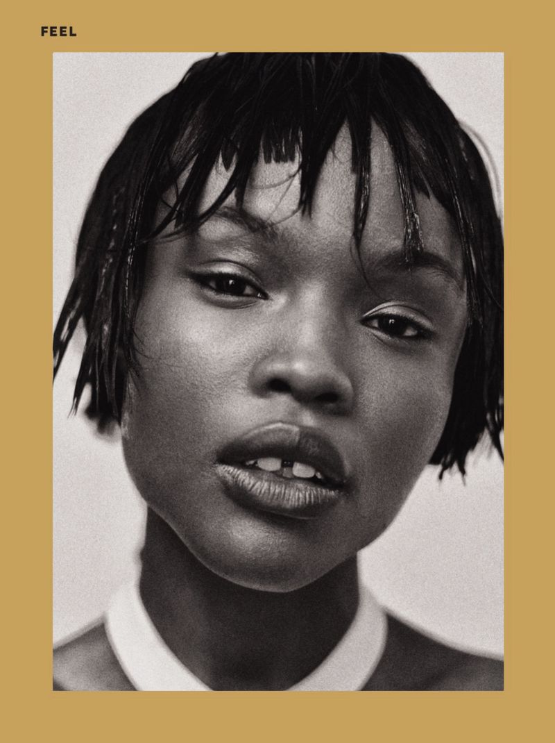 Monochrome portrait of a young Black woman with wet short black hair, gazing at the camera against a beige-grey background and white top.