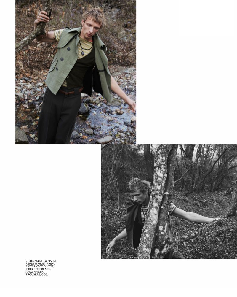 A man wearing a vest and trousers poses outdoors in a forest near a creek in a black and white and color fashion shot.