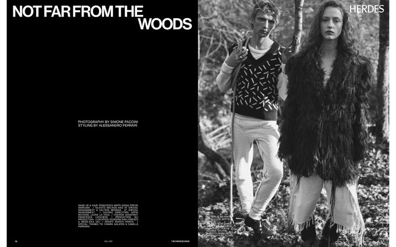 Black and white fashion shot with two posed adults in a forest setting, featuring patterned sweaters and fringed outerwear.