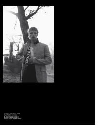 Black and white editorial photograph of a male model wearing a tailored jacket outdoors near a tree.
