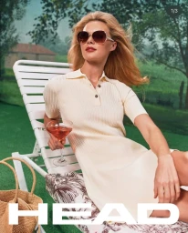 Model wearing sunglasses and a cream polo dress sitting on a white lounge chair holding a cocktail glass with a green backdrop.
