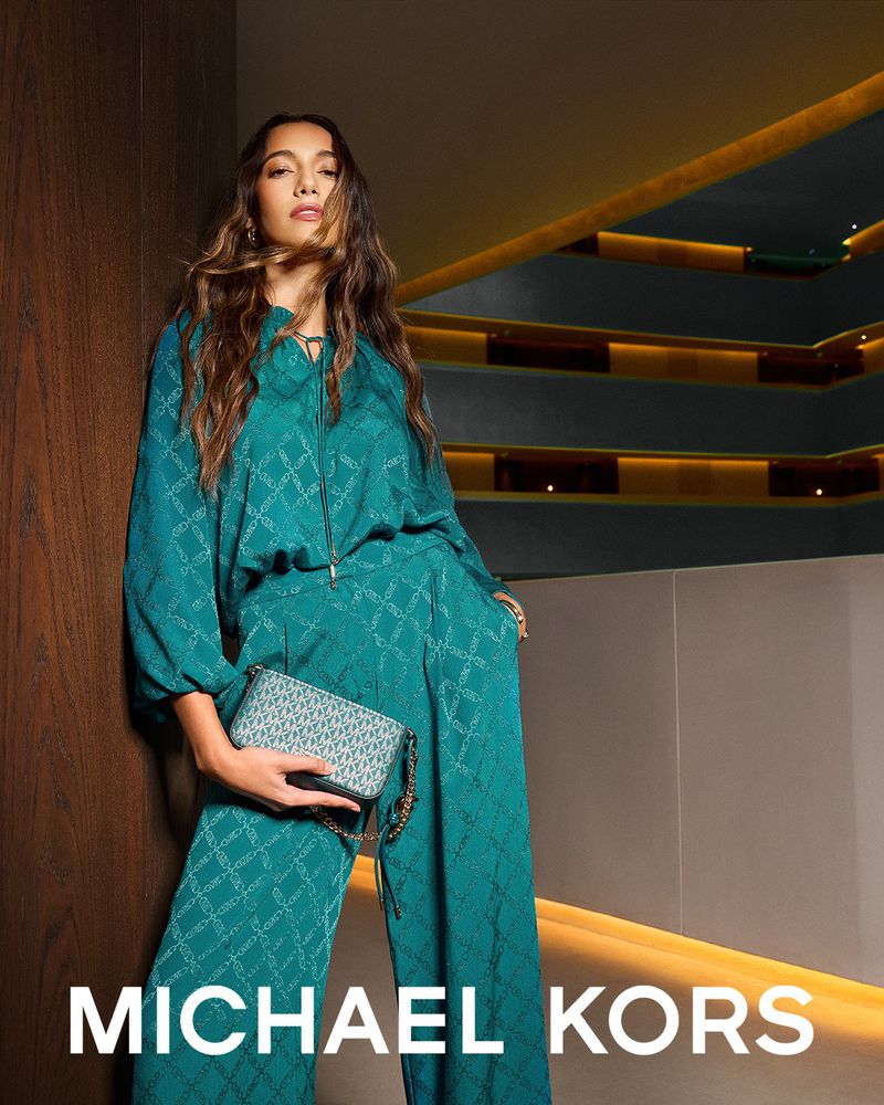 A woman poses in a teal matching set with a patterned purse; brand logo visible in the lower portion of the frame.