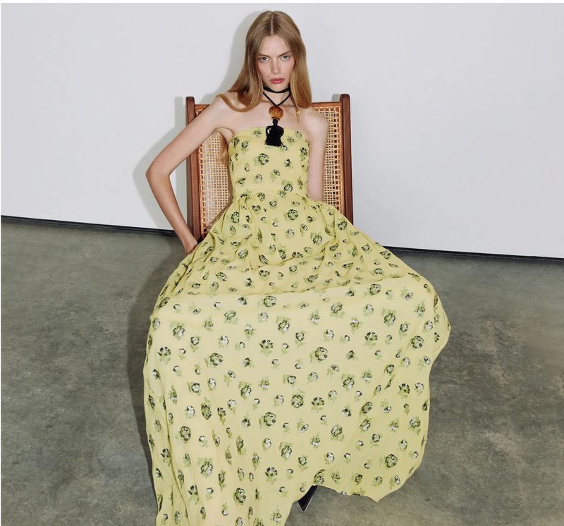Model seated in a cane-backed chair wearing a yellow floral maxi dress for Tanya Taylor Spring 2026.