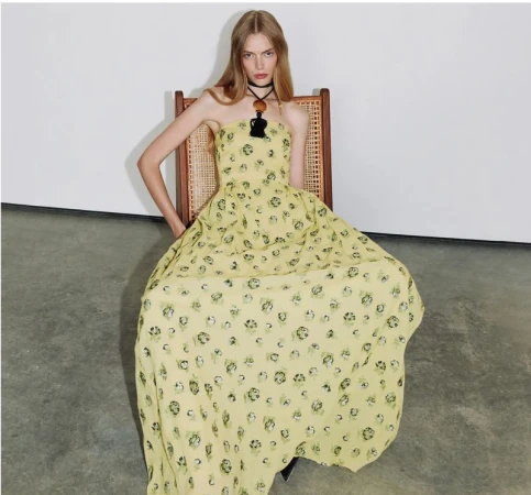 Model seated in a cane-backed chair wearing a yellow floral maxi dress for Tanya Taylor Spring 2026.