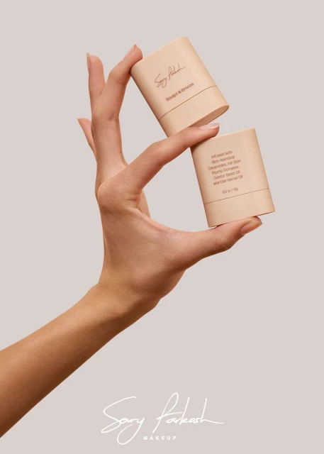 Cosmetic sticks are held in a human hand against a neutral background in a beauty and product photography studio shot.