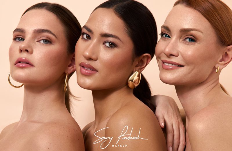 Beauty shot of three diverse women with perfect makeup, radiant skin, and gold hoop earrings against a neutral backdrop, showcasing beauty and style.