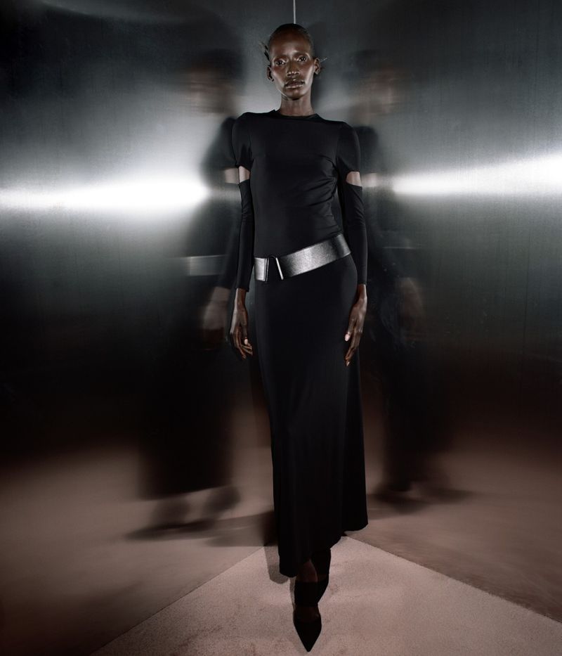 Elegant Black woman in a black gown with a metallic belt stands against a dark, reflective background, showcased with creative motion blur.